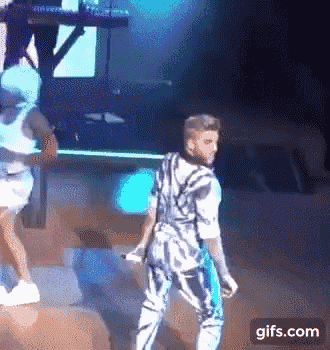 a man is dancing on a stage while holding a microphone and a woman is standing behind him .