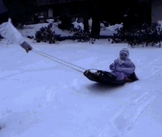 a little girl is being pulled down a snow covered hill on a sled