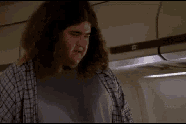 a man with long hair is sweating while talking on a cell phone on an airplane .