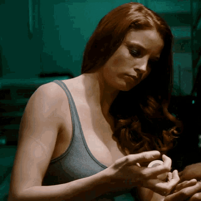 a woman in a grey tank top is holding something in her hand