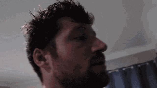 a close up of a man 's face with a beard and a blue curtain in the background