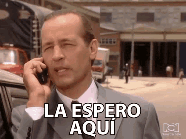 a man in a suit talking on a cell phone with la espero aqui written on the bottom