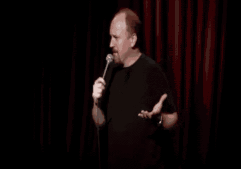 a man is holding a microphone in front of a red curtain on a stage .