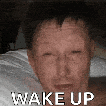 a man is laying on a bed with his eyes closed and the words wake up written on his face .