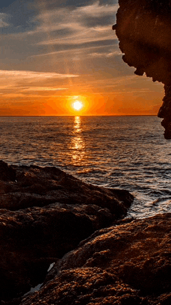 a sunset over a body of water with a rocky shoreline in the foreground
