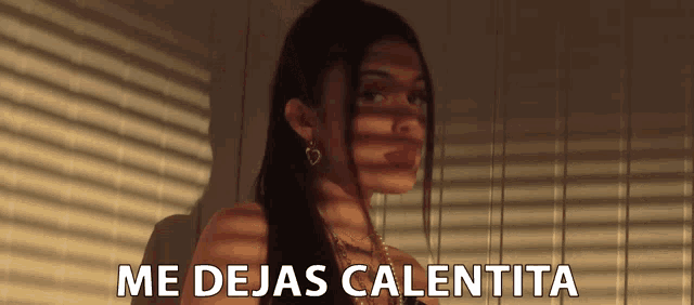 a woman is standing in front of a window with the words me dejas calentita written below her