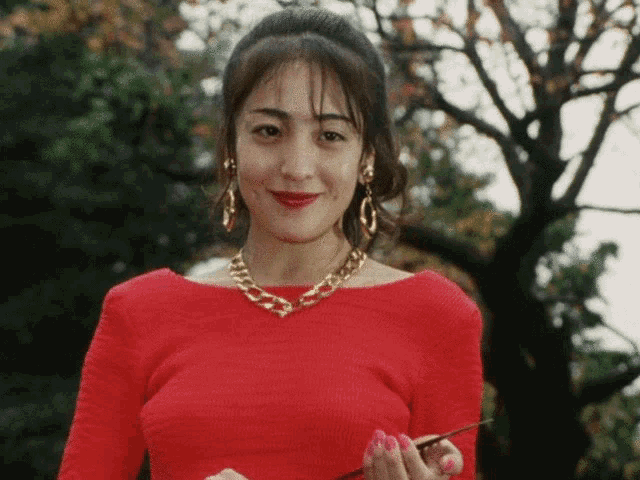 a woman in a red top and gold chain necklace smiles