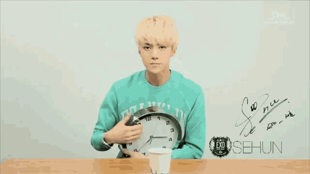 a person holding a clock in their mouth and a cup of coffee in front of a sign that says sehun