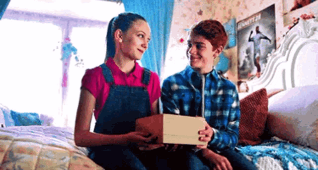 a boy and a girl are sitting on a bed looking at each other . the boy is holding a box .