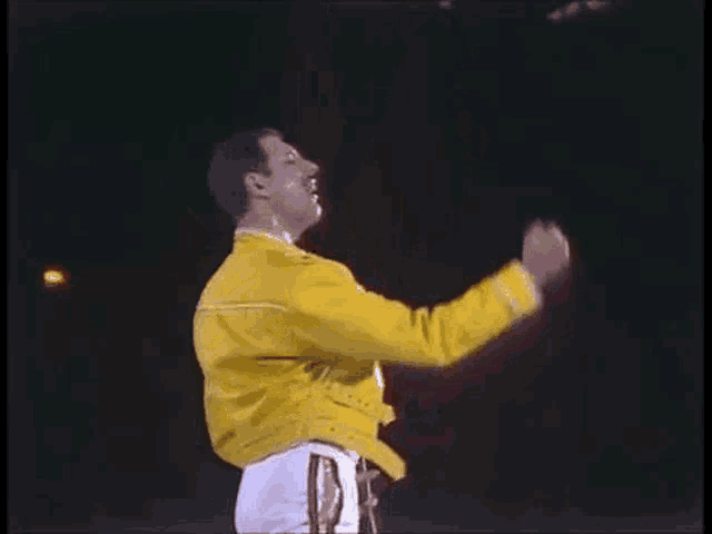 a man in a yellow jacket is raising his arms in the air .