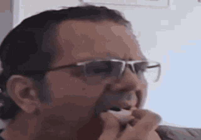 a man wearing glasses is eating a piece of bread .