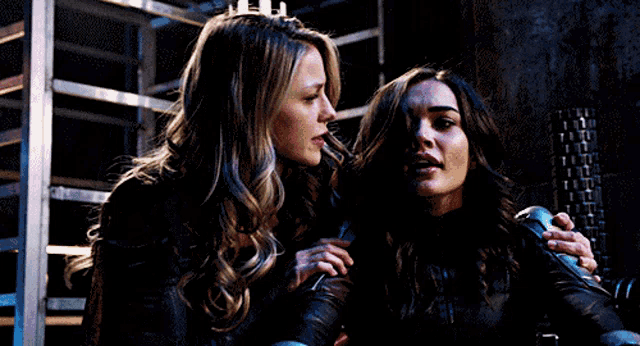 two women are standing next to each other in a dark room and looking at something