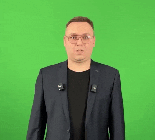 a man wearing glasses and a suit is standing in front of a green screen .