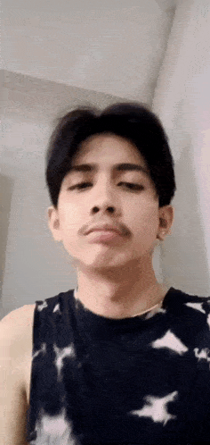 a young man with a mustache is making a funny face while wearing a tie dye tank top .