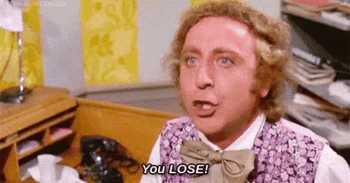 a man in a purple vest and bow tie is saying `` you lose '' while sitting at a desk .