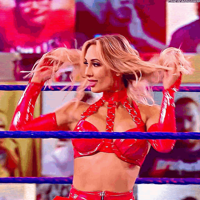 a woman in a red outfit is standing in a wrestling ring holding her hair