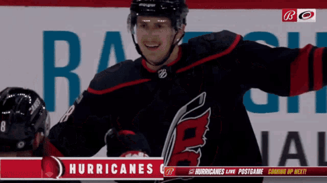 a hockey player stands in front of a banner that says hurricanes on it