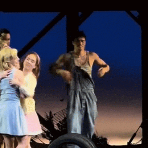 a man in overalls is standing on a tire surrounded by women