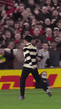 a man in a black and white striped shirt is running on a field
