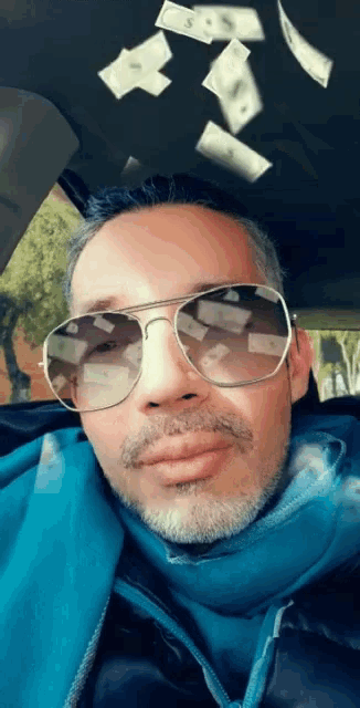 a man wearing sunglasses is sitting in a car while money is falling from the ceiling