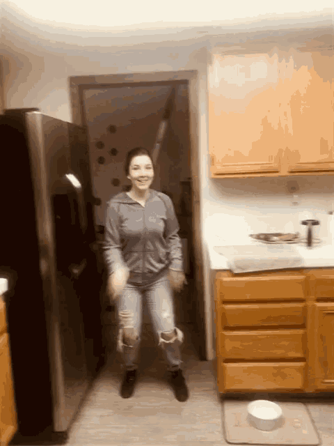 a woman is dancing in a kitchen in front of a fridge