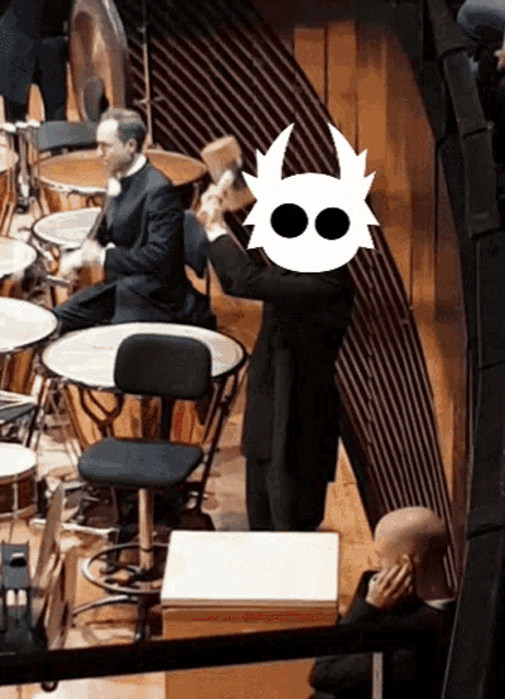 a man in a suit holds a hammer in front of a drum set