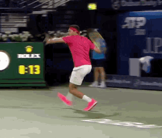 a man in a pink shirt is swinging a tennis racquet in front of a scoreboard that says rolex