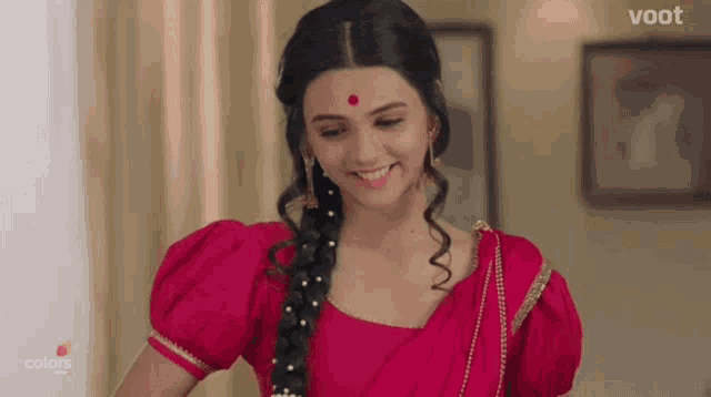 a woman wearing a red blouse and a red dot on her forehead is smiling .