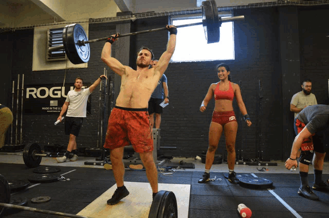 a man lifts a barbell over his head in front of a rogue sign