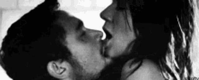 a black and white photo of a man and a woman kissing .