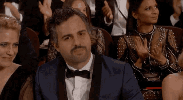 a man in a tuxedo sits in a crowd of people