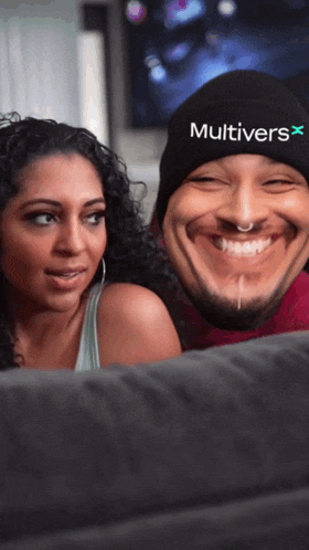 a man wearing a beanie with the word multivers on it smiles next to a woman