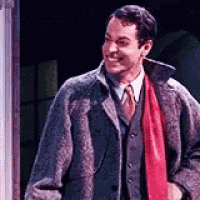 a man in a suit and tie with a red scarf around his neck is standing in front of a door .