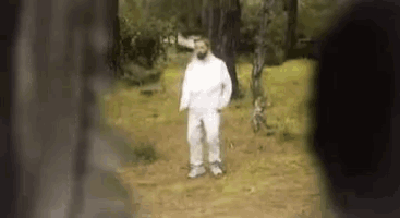 a man in a white jumpsuit is standing in the woods .