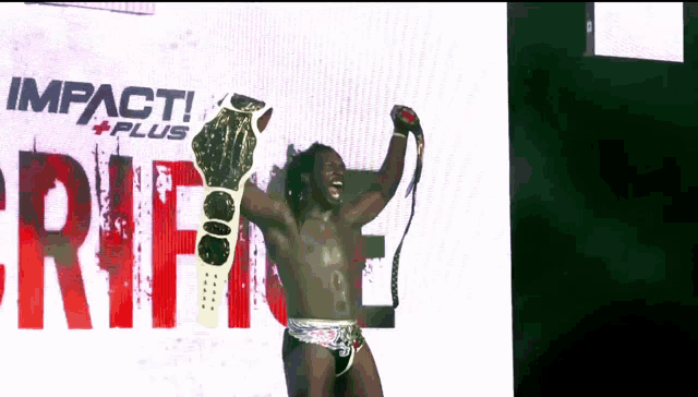 a man is holding a wrestling championship belt in front of a large screen that says impact plus
