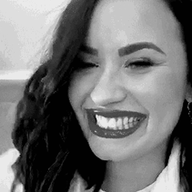 a black and white photo of a woman smiling with red lipstick on her lips .