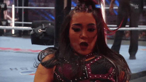 a woman is standing in a wrestling ring with her mouth open and a w logo in the background