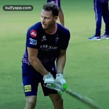 a man in a blue shirt and shorts is holding a bat on a field .