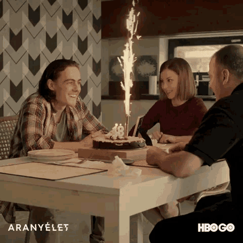 a group of people sitting at a table with a birthday cake with candles on it and the words aranyelet on the bottom