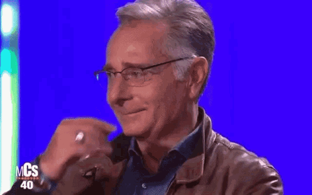 a man wearing glasses and a leather jacket is covering his mouth with his hand ..