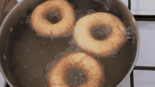 three donuts are frying in a pot of boiling water .