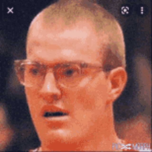 a close up of a man wearing glasses and a shaved head .