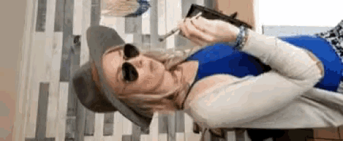 a woman wearing a hat and sunglasses is smoking a cigarette while laying on a table .