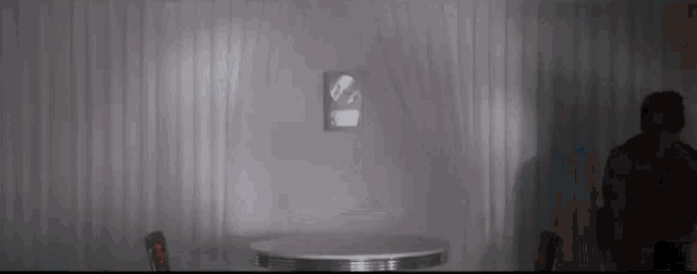 a man is standing in front of a table in a dark room with a clock on the wall .