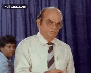 a bald man wearing glasses and a white shirt is standing in front of a blue curtain .