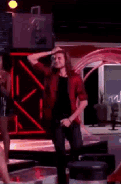 a man in a red shirt is dancing on a stage in front of a woman in a black dress