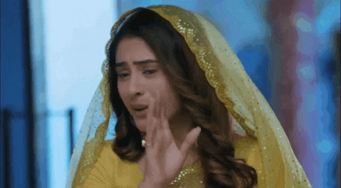 a woman in a yellow dress and veil is crying and covering her face with her hand .