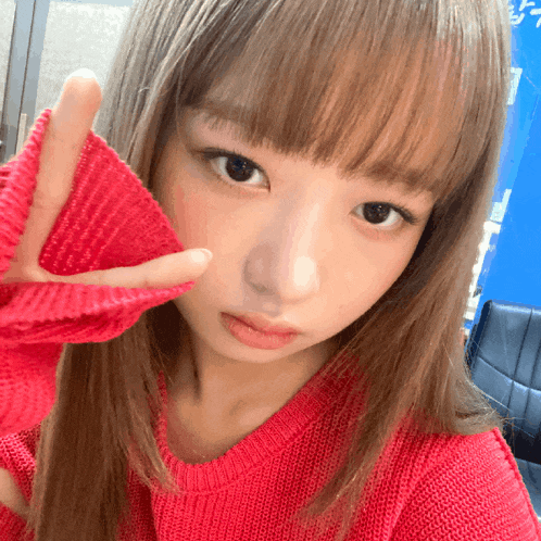 a woman in a red sweater is making a peace sign with her hand