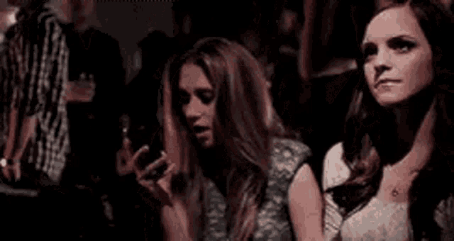 two women are dancing in a club while one of them is looking at her phone .