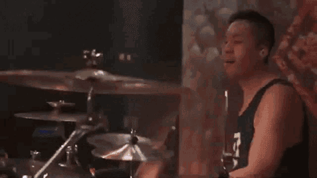 a man in a tank top is playing drums in front of a purple background